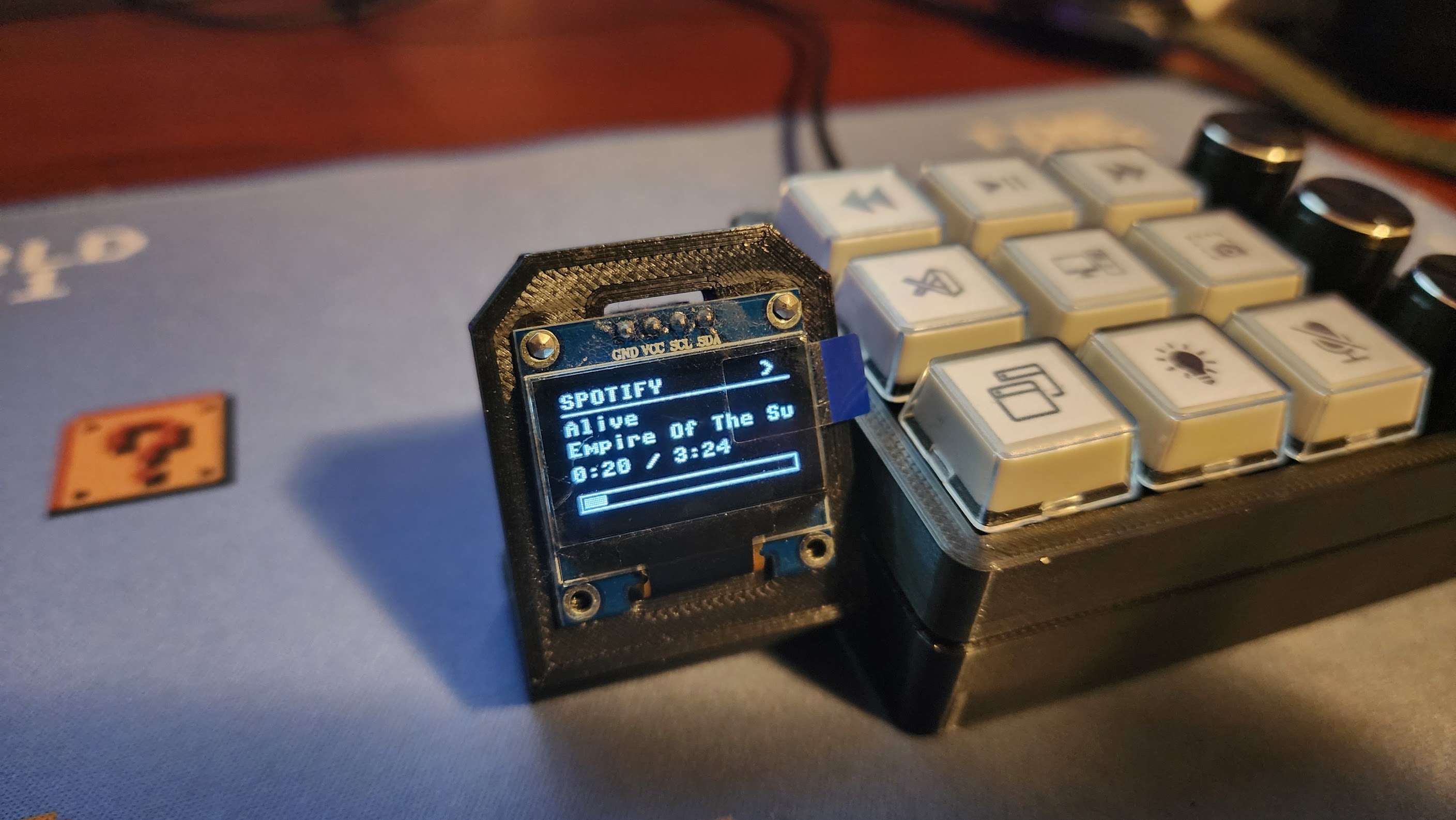 Macro controller OLED displaying Spotify now-playing information